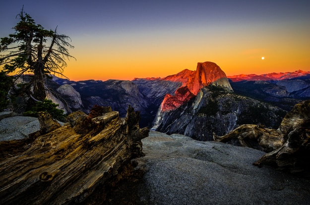 A full moon rises behind iconic Half Dome at sunset from Glacier Point in Yosemite National Park