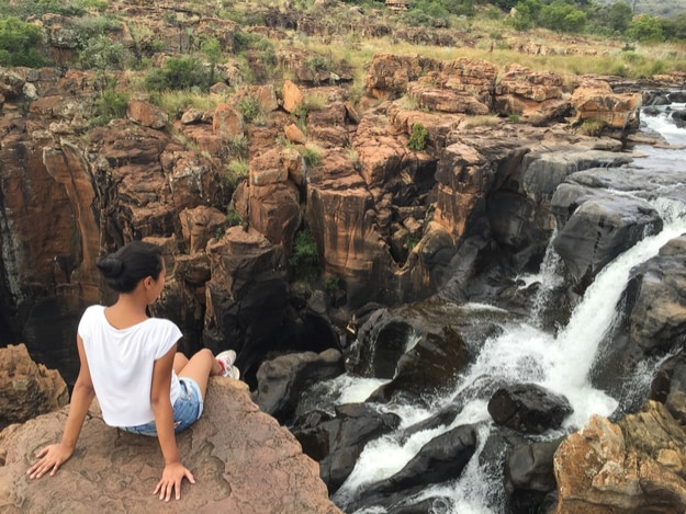 Girl sitting in a rock overlooking a waterfall in a rocky landscape at Blyde River Canyon in South Africa