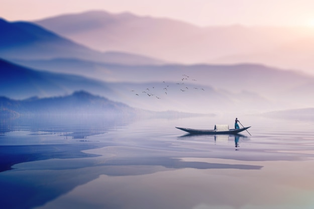 man riding boat in a foggy winter morning infront of a beautiful mountain in lake in Bangladesh