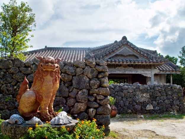 A traditional Okinawan house with large tiled roof,and shisa a traditional Ryukyuan decoration, often in pairs, resembling a cross between a lion and a dog.