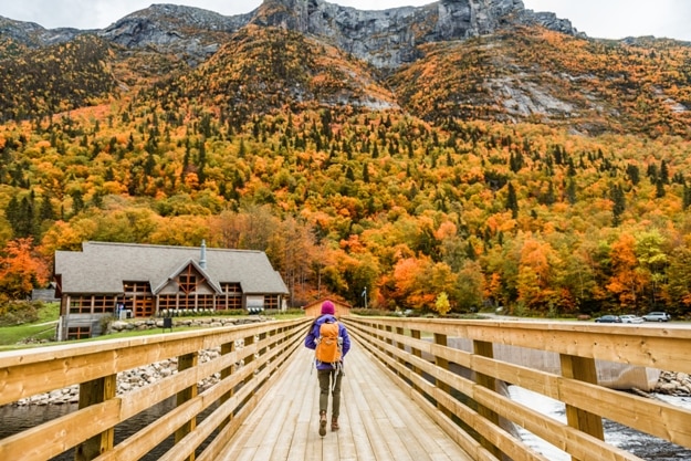 Autumn nature hiker girl walking in national park in Quebec with backpack. Woman tourist going camping in forest. Canada travel hiking tourism at Hautes-Gorges-de-la-Riviere-Malbaie National Park