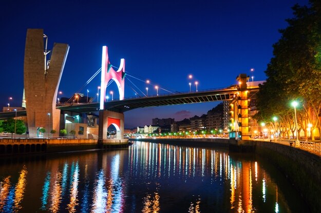 Bilbao, Spain. Illuminated Salbeko zubia Bridge over Nevion River in Bilbao, Spain at night. Lights reflection in the water, buildings at the background and clear dark blue sky