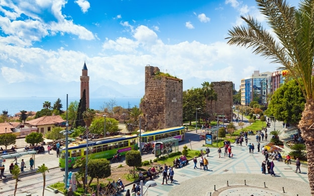 People walking near Clock Tower, Tekeli Mehmet Pasa Mosque and Yivli Minare Mosque or Alaaddin Mosque located in Kaleici district old town center of Antalya, Turkey