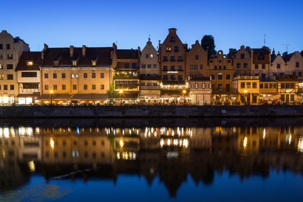 Scenic view of lit old buildings along the Long Bridge waterfront and their reflections on the Motlawa river at the Main Town in Gdansk, Poland, in the evening